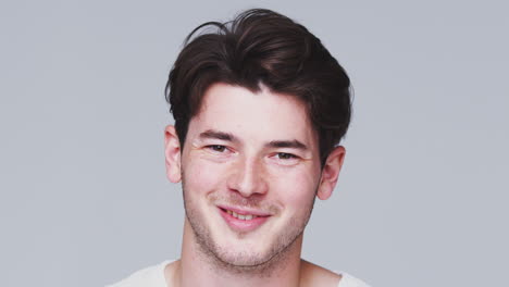 head and shoulders studio shot of young man smiling at camera in slow motion