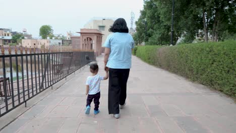 Madre-Joven-Sosteniendo-El-Dedo-De-Su-Hijo-Pequeño-Y-Caminando-Al-Aire-Libre-Por-La-Noche