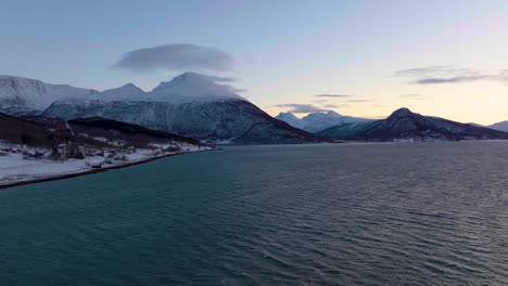 picturesque landscape of sea, snowy mountain, and arctic village at polar night in northern norway