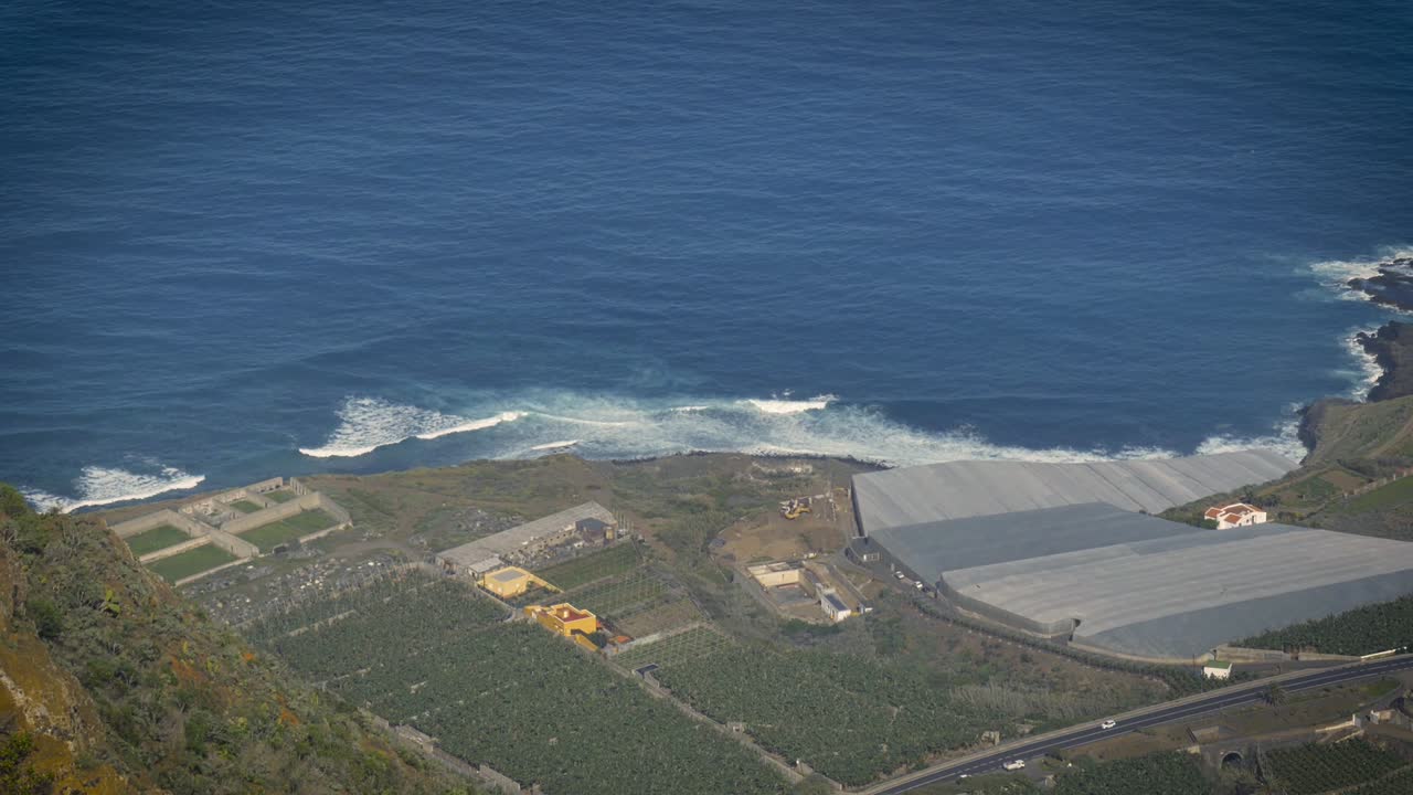 costa escarpada de tenerife, islas canarias y granja, vivero de plantas a lo largo de la costa con océano azul y olas rompiendo en la costa
