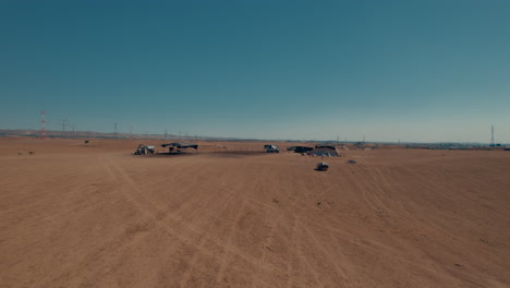 Bedouin-residential-tents-without-a-permit-in-a-remote-and-desert-area,-near-a-highway-and-large-power-poles,-dry-land-without-crops,-push-in-shot-1