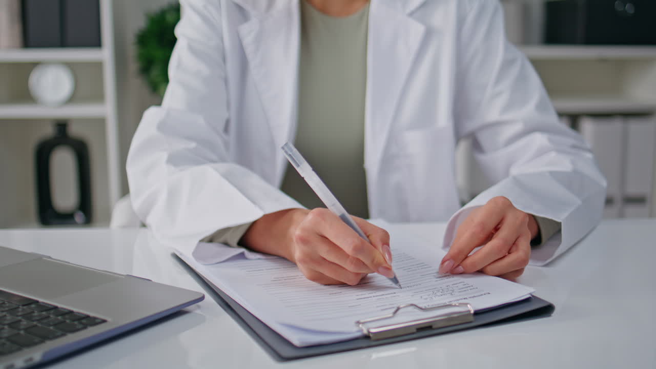 Physician hands writing records sitting clinic table with laptop closeup