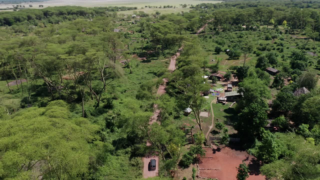 Aerial drone shot flying forward following a van driving in a gravel road surrounded by trees in Tanzania. Clear blue sky