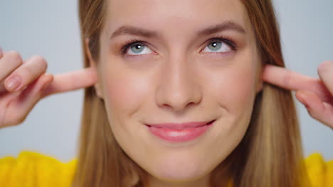 Closeup-smiling-woman-covers-her-ears-with-fingers-at-camera-in-studio.