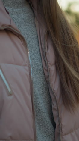 un primer plano de una chica sonriente con una chaqueta de melocotón y de pie en patines en un parque. el fondo está suavemente borroso, expresión feliz y la luz suave que se refleja en su cabello