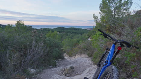 mountain bike parked on dirt track leading downhill toward stunning early morning sky and sea views at horizon