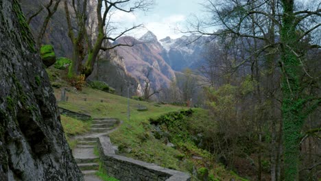 Un-Panorama-De-Un-Valle-Montañoso,-Donde-Los-Picos-Están-Cubiertos-De-Nieve,-Los-árboles-Desnudos-Permanecen-Quietos-En-El-Aire-Sin-Viento-Y-Un-Automóvil-Solitario-Conduce-Por-La-Carretera