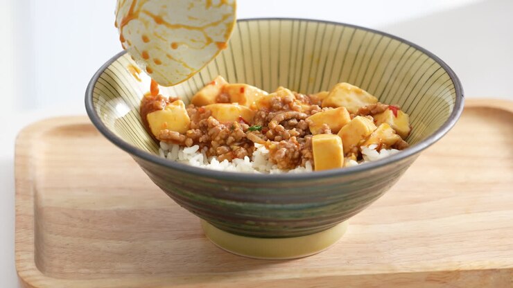 Pouring stir-fried mapo tofu with hot spicy sauce over white rice in a bowl at home