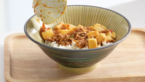 pouring stir-fried mapo tofu with hot spicy sauce over white rice in a bowl at home