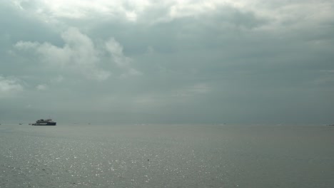 timelapse static shot of a sea with a big ship and isolated small boats while the clouds pass by quickly in calm waters