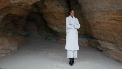 unhappy girl thinking troubles at seashore cave. lonely woman with crossed hands