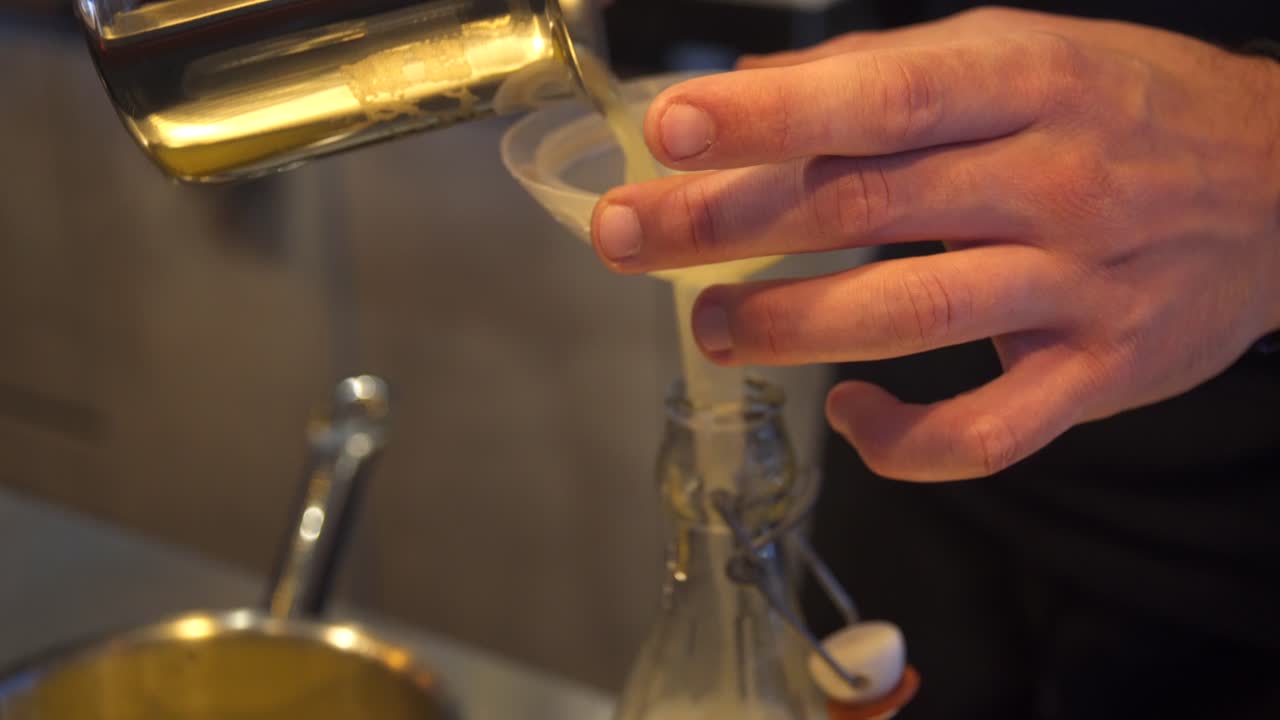 vista lateral de cerca 4k disparado en las manos del camarero vertiendo jugo de limón en una botella a través de un embudo de plástico