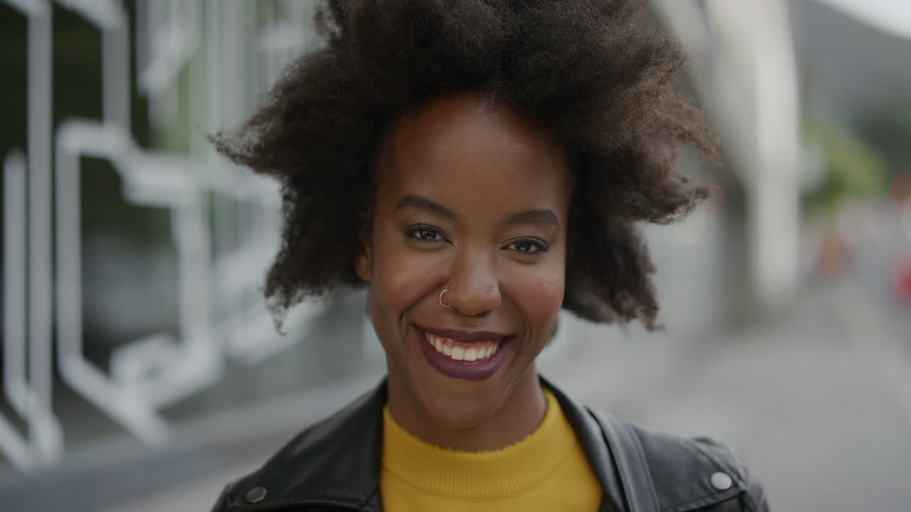 retrato de una mujer afroamericana segura sonriendo alegremente mirando a la cámara en el fondo de una ciudad urbana vibrante joven estudiante con afro funky en cámara lenta