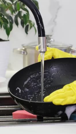 a woman in yellow gloves washes a pan