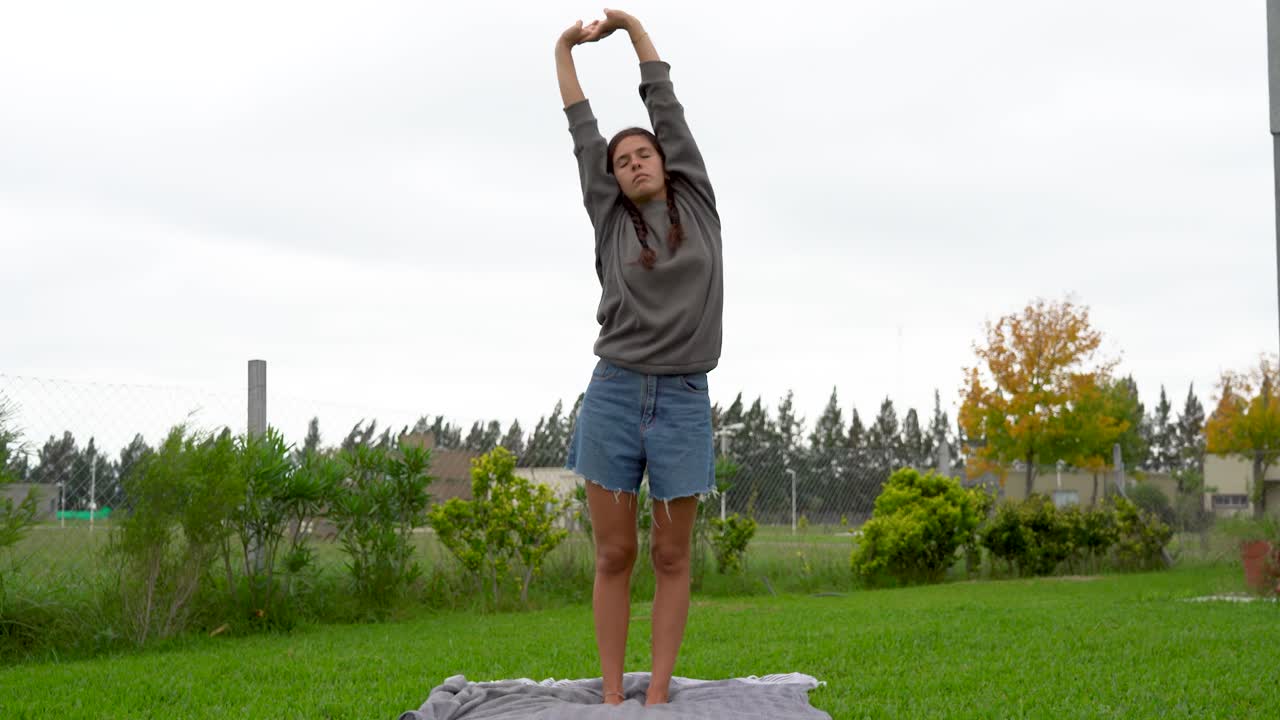 mujer joven se para y se estira en la manta en el césped en un día nublado, tiro completo