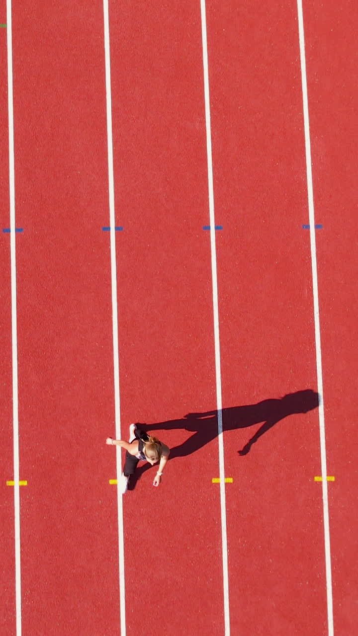 Vista aerea dall'alto di un'atleta donna che scatta su una pista rossa in uno stadio. Perfetta per contenuti di fitness, sport e motivazionali