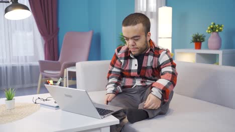 joven enano frustrado y agotado trabajando desde casa en la computadora.