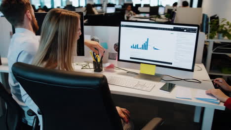 People working in a modern open-plan office environment with computers and data displays