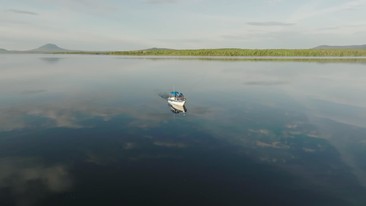 un barco solo cruzando un lago plano y tranquilo que refleja las nubes