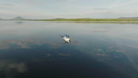 a boat alone crossing flat calm lake reflecting clouds