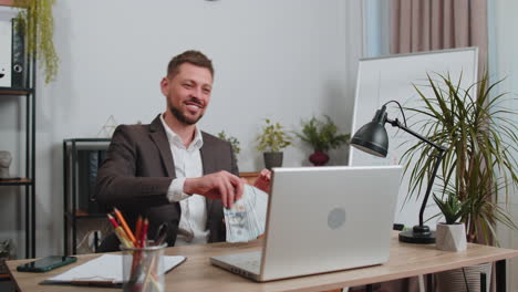 Un-Hombre-De-Negocios-Alegre-Trabajando-En-Una-Computadora-Portátil-De-Oficina-Regocijándose-Por-Ganar,-Recibiendo-Dinero-En-Efectivo,-éxito,-Suerte-De-Lotería