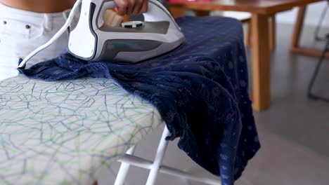 a person irons a blue garment on a patterned board in a bright, modern room