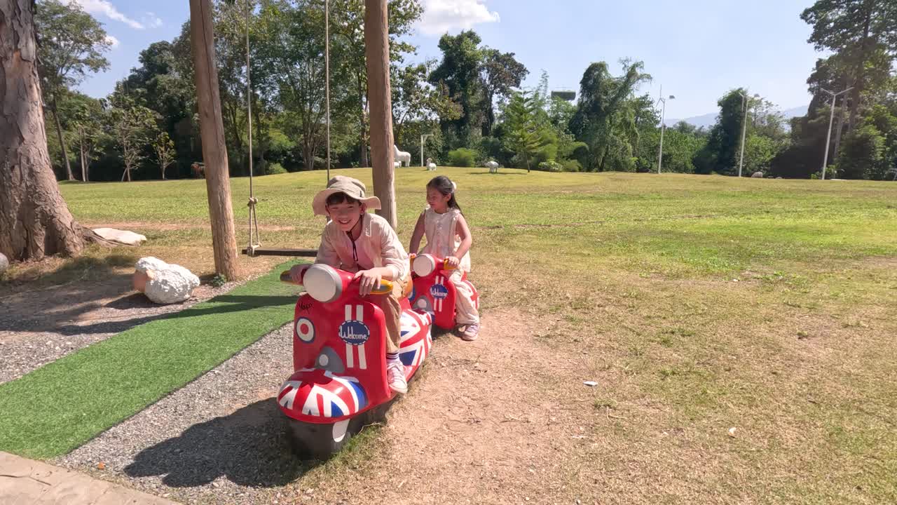 Bambini piccoli giocano su un monopattino rosso fisso in un parco soleggiato di Khao Yai