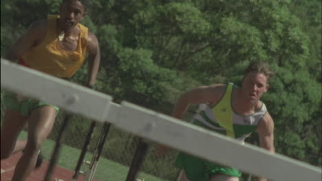 Two-athletes-race-down-a-track-jumping-hurdles