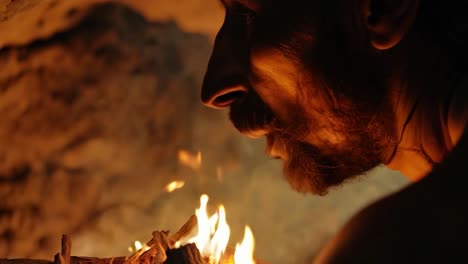 a man blowing on a small fire in a dark cave