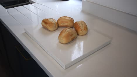 modelo femenino deslizando panecillos calientes sobre una encimera de cuarzo en una cocina moderna