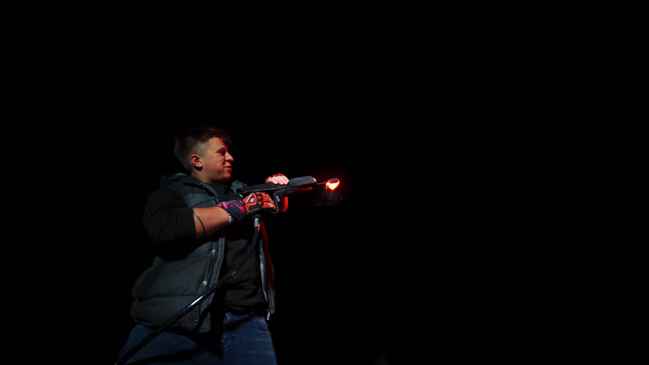 Man shooting from a fire gun at night outdoors. Bright fire show at black backdrop.