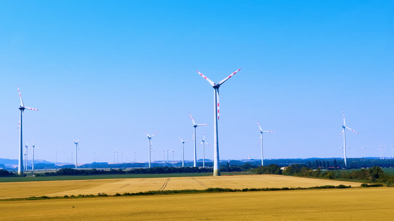 Le turbine producono energia nei campi. Le turbine eoliche si ergono alte in un ampio campo, ruotando lentamente sotto un cielo azzurro mentre generano energia rinnovabile.