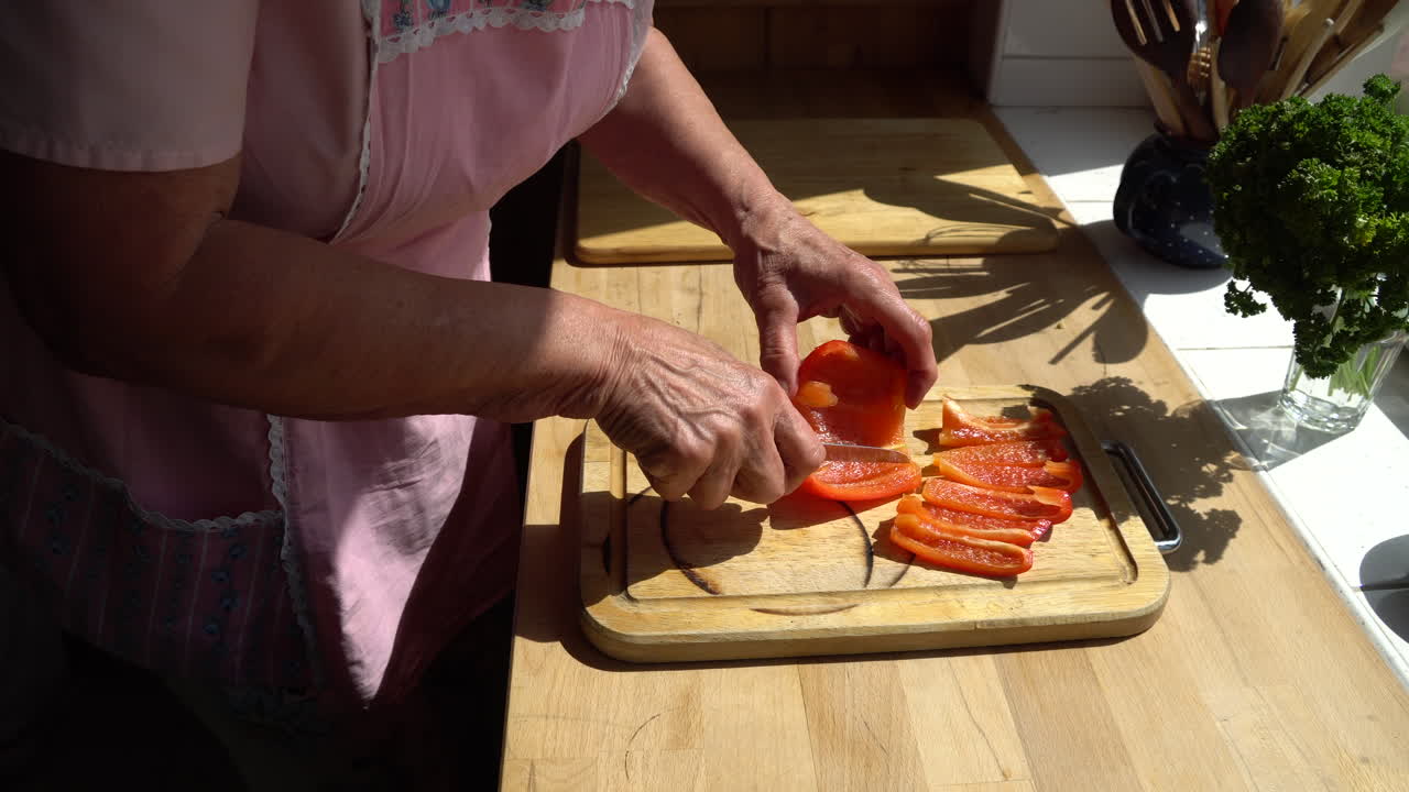 señora mayor cortando paprika en la cocina en una tarde soleada