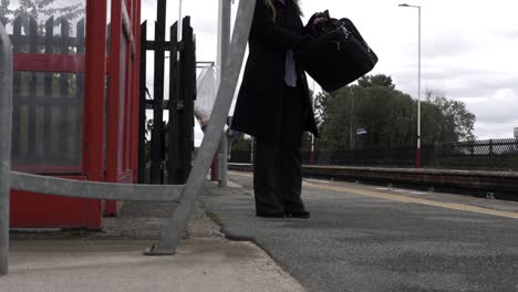 business woman waiting at train station putting documents in briefcase wide shot