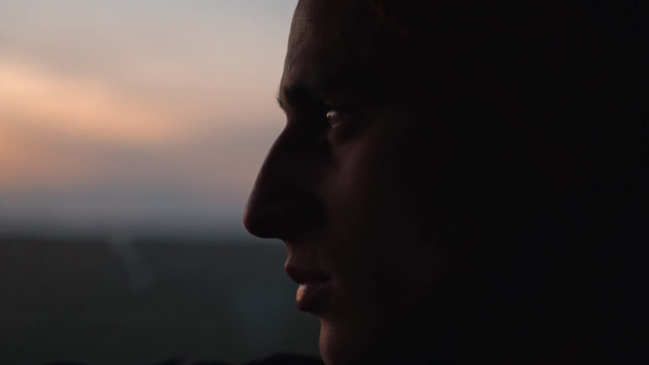 A man's silhouette is cast against the beautiful, blurred colors of an Icelandic sunset as he gazes out through a window, capturing a serene and reflective moment during a road trip
