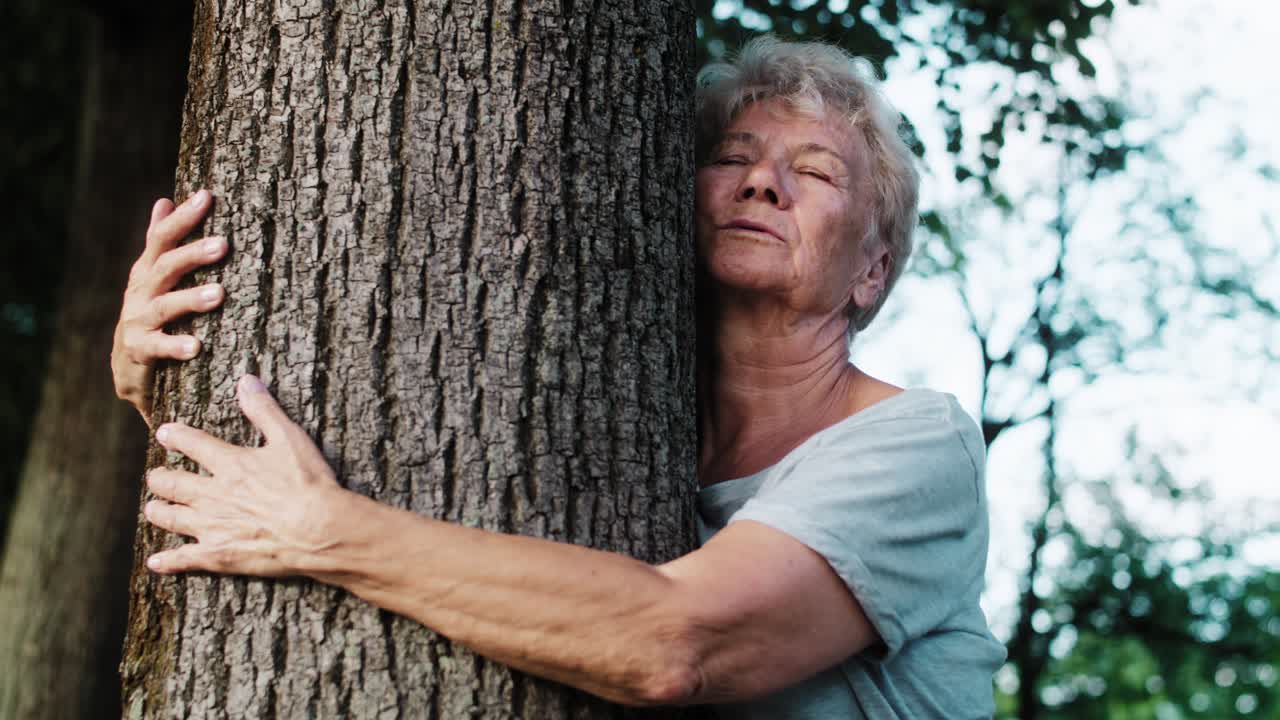 Calm senior woman doing breathing exercise next to the tree in the park
