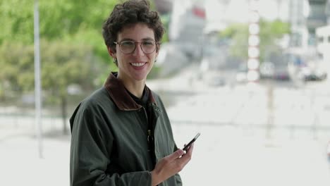 Woman-holding-smartphone-and-smiling-at-camera