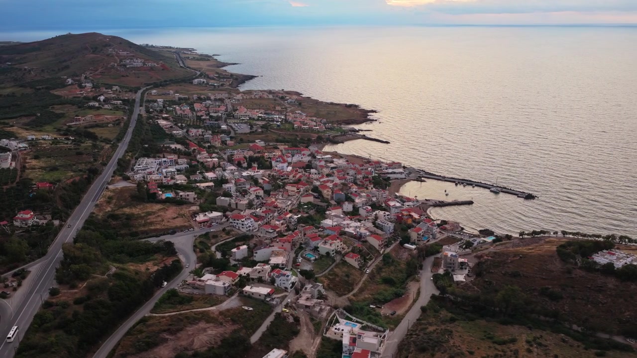 Luftfoto fra drone af en kystby og havn ved siden af en bar odde ved solnedgang, Panormos, Grækenland.
