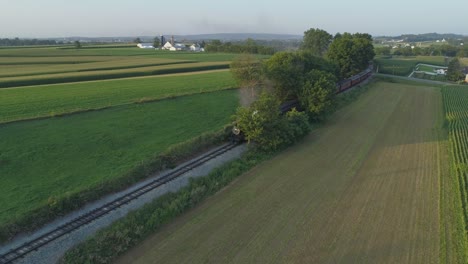 Luftaufnahme-Einer-Dampfmaschine-Von-1924-Mit-Einem-Personenzug,-Der-Entlang-Der-Amish-Landschaft-Fährt,-Während-Die-Sonnenuntergänge-An-Einem-Sommertag-Von-Einer-Drohne-Gesehen-Werden