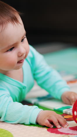 curious caucasian baby boy lying on the floor reaching a ball. sweet kid takes a toy and bangs it by the floor. vertical video
