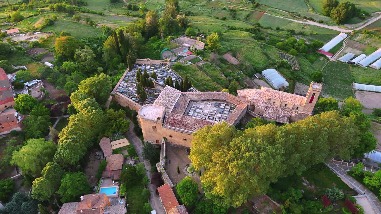 Aerial orbit of the fortified cemetery and Romanesque church of Brihuega, in La Alcarria, Spain. Surrounded by trees and farmland, this clip shows rich textures and historic architecture at sunrise