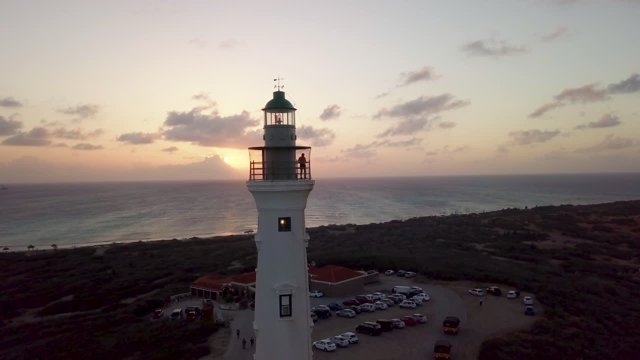 un hombre toma fotos de aruba desde lo alto del faro de california durante una hermosa puesta de sol naranja