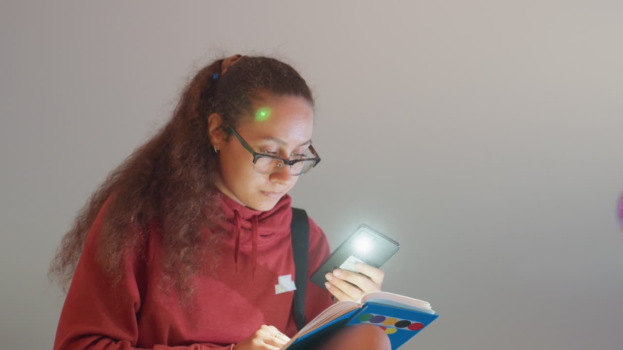 Night rooftop writer holding phone light and notebook, focused note taking under soft skyline glow, red hoodie and glasses, reflective mood, creative concentration and idea capture