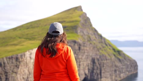 mujer con sombrero en el acantilado de traelanipa admirando las montañas volcánicas feroesas en vagar, islas feroe