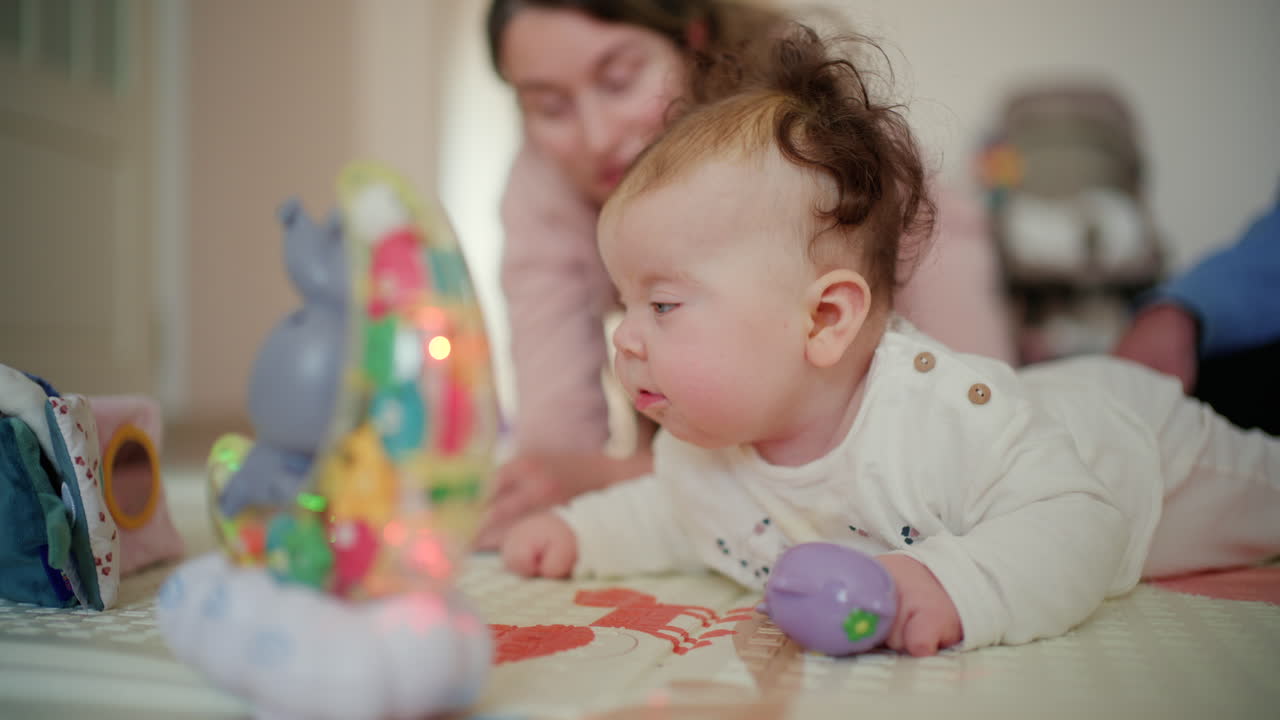 Bebê praticando engatinhar e brincando com brinquedos em um tapete macio, com a mãe supervisionando ao fundo.