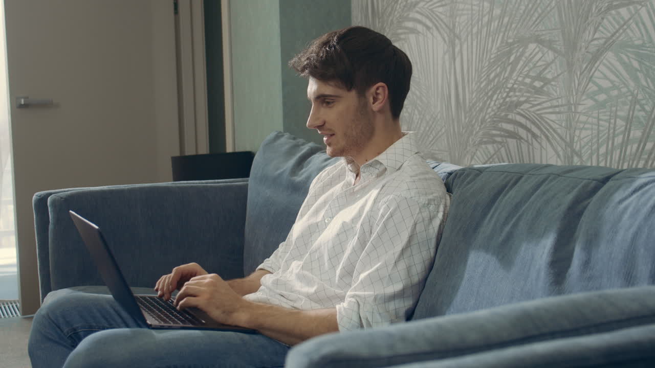 hombre sonriente leyendo mensajes en la computadora. hombre feliz sentado en el sofá con una computadora portátil.