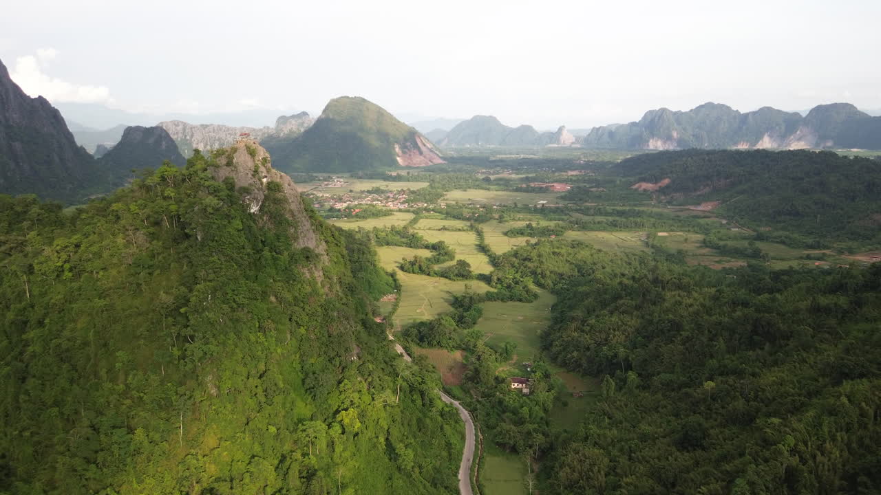 Mountain ridges and rice fields around Vang Vieng panoramic aerial dolly at serene high angle with rolling hills