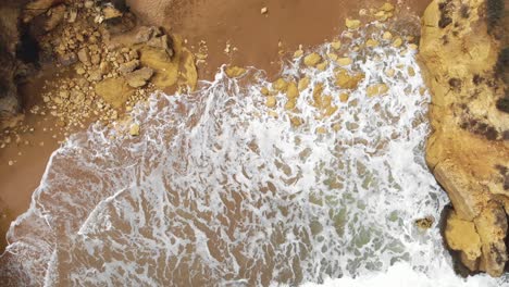 Aerial-top-view-of-ocean-waves-break-on-a-rocky-sand-beach