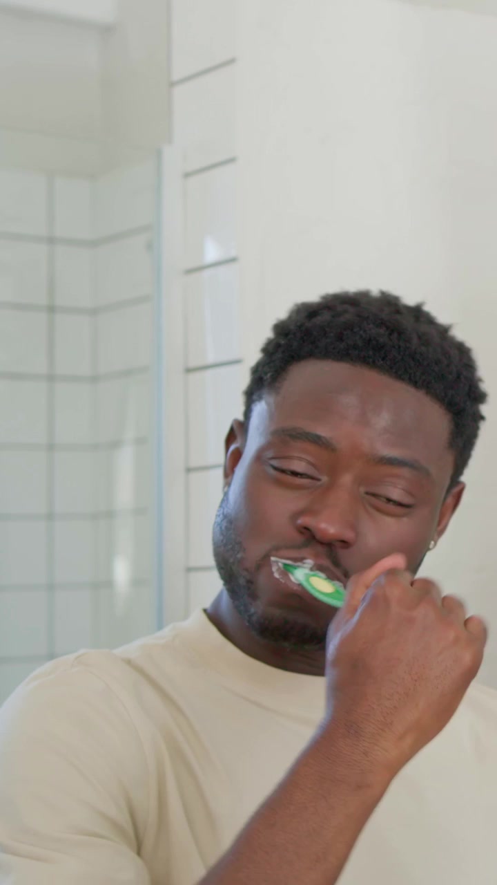 Vertical video: Gripping toothbrush man brushing teeth in bathroom making foam to clean mouth
