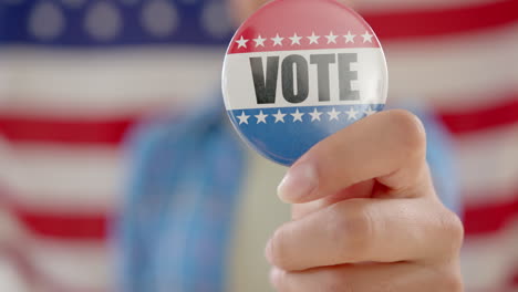 hand of biracial teenage girl agaisnt american flag holding vote badge, slow motion